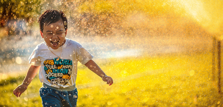 niño con ropa de verano corriendo por el campo mientras le salpica agua y se ríe feliz