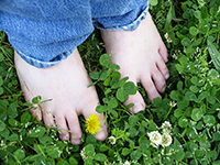 Pies de niño pequeño descalzos sobre la hierba, con pantalón vaquero