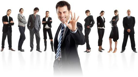 Grupo de personas mixto al fondo con ropa oscura típica de trabajadores de oficina y hombre de mediana edad en primer plano, con traje y corbata a rayas, mirando a la cámara y haciendo el signo de OK con la mano izquierda